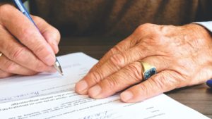 An oder man's hands singing a document representing a Will
