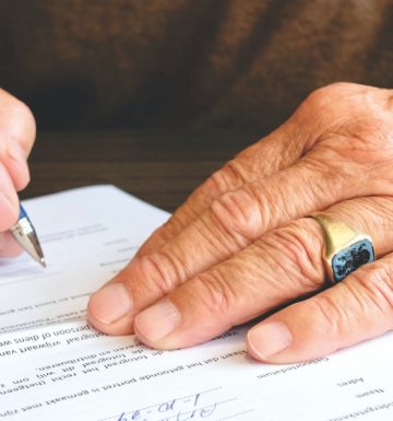 An oder man's hands singing a document representing a Will